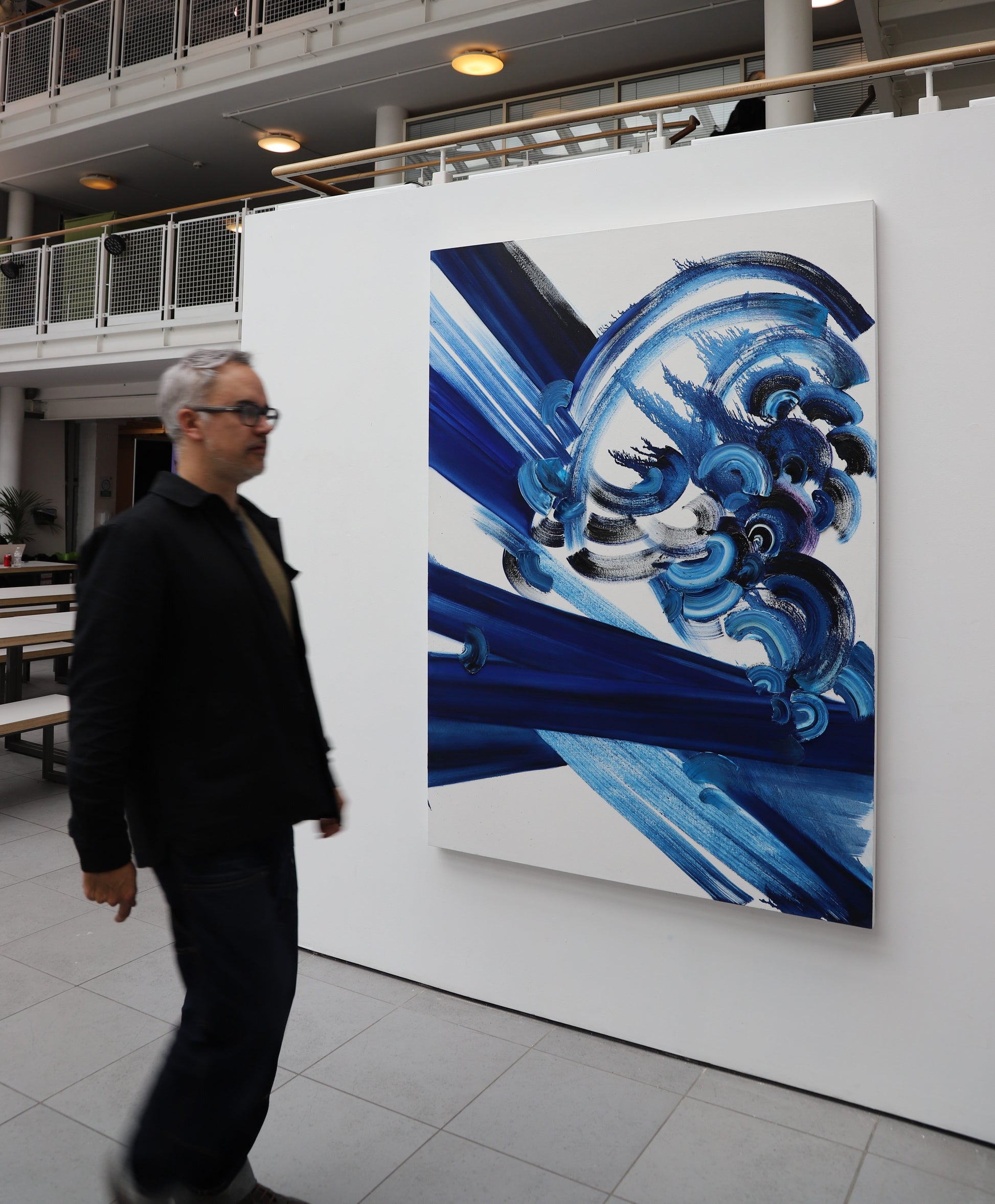 Abstract artwork 180 x 130 cm. with blue and black brush strokes with a white background in indoors setting