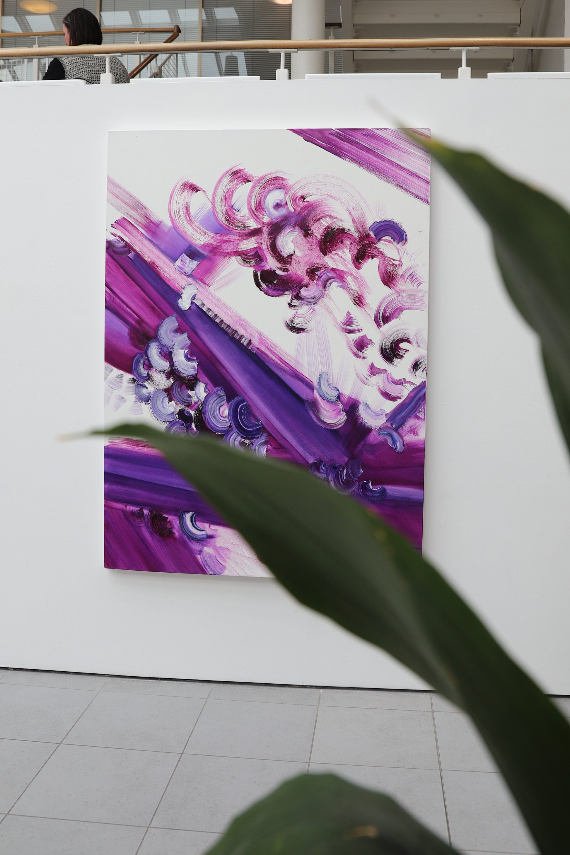 Colorful abstract painting on a white wall with plant leaves in the foreground