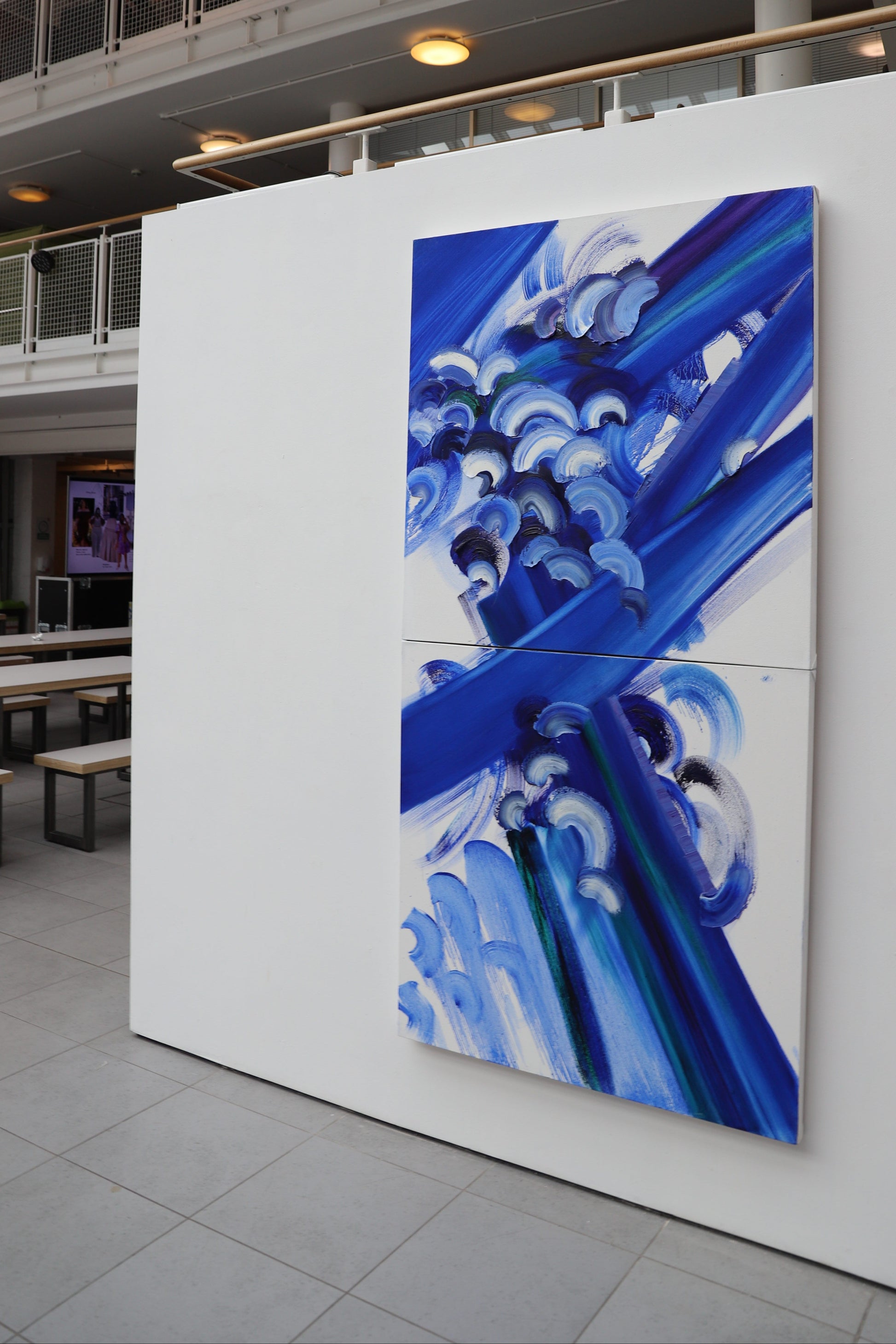 Abstract artwork with blue and white patterns on a white wall in an indoor setting.