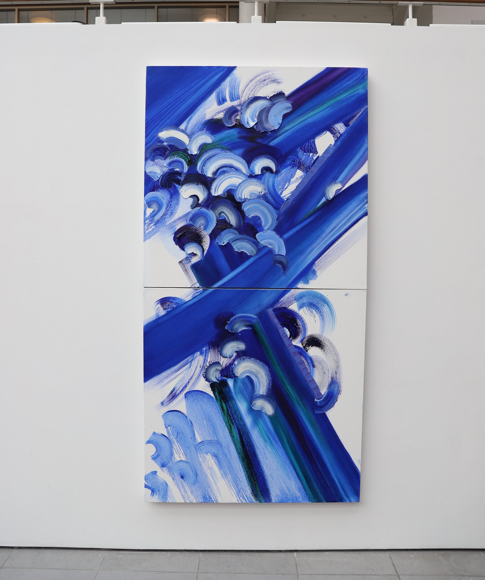 Abstract art piece with blue and white patterns on a white wall.