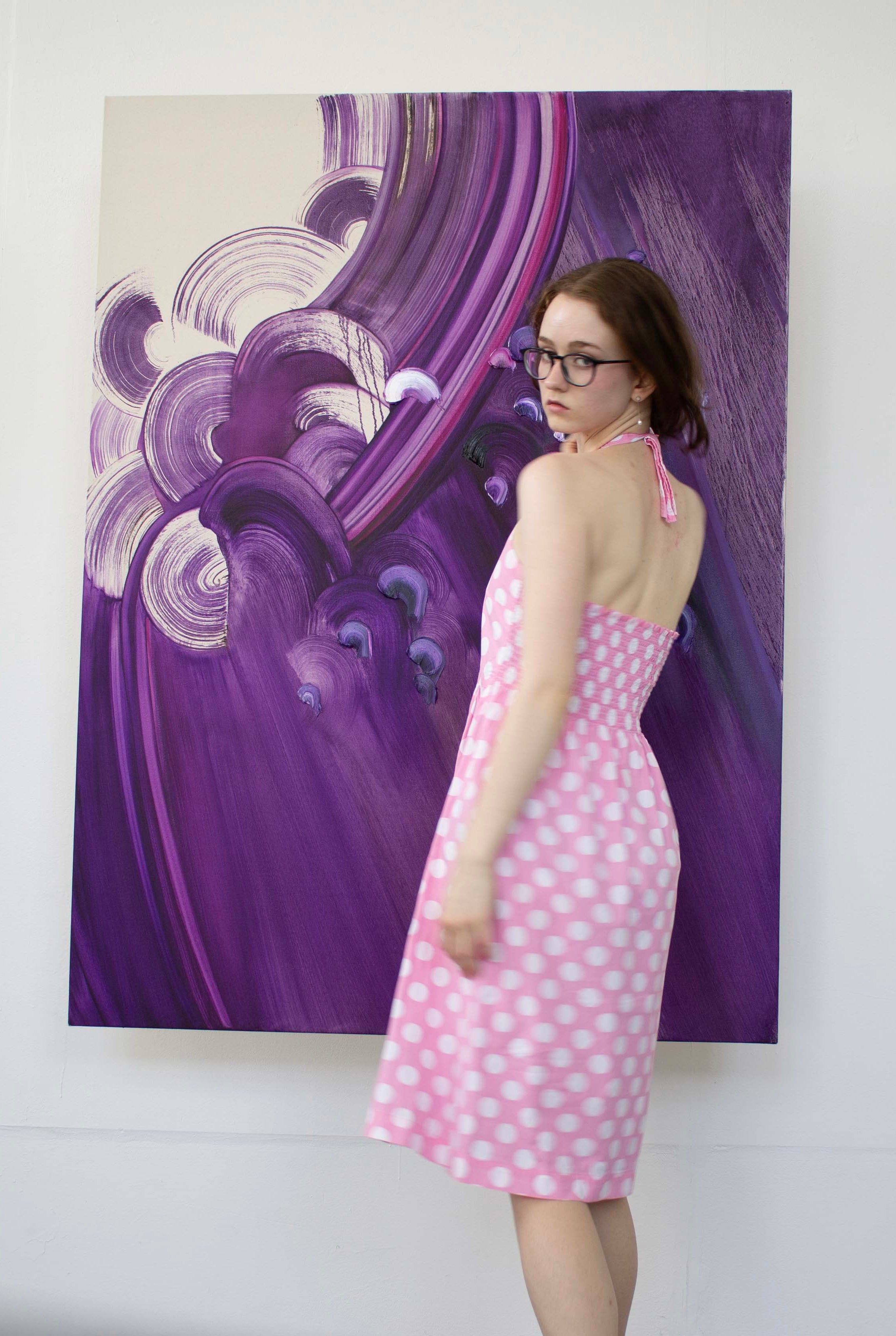 Woman in a pink polka dot dress standing in front of a large abstract painting.